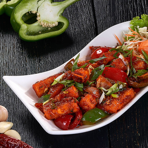A colorful dish of Chilli Paneer with bell peppers, onions, and a spicy sauce at an Indian Restaurant