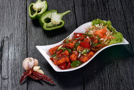 A colorful dish of Chilli Paneer with bell peppers, onions, and a spicy sauce at an Indian Restaurant